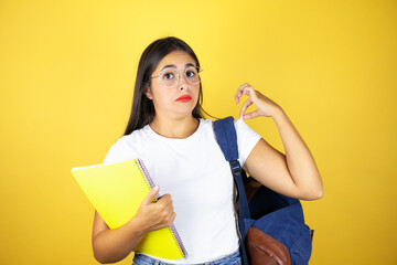 Young beautiful student woman wearing backpack holding notebook over isolated yellow background with a successful expression