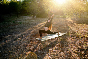 Young girl is doing yoga strethching on the mat on the olive grove at sunset. Female yoga training for stay healthy, mental and fisical health
