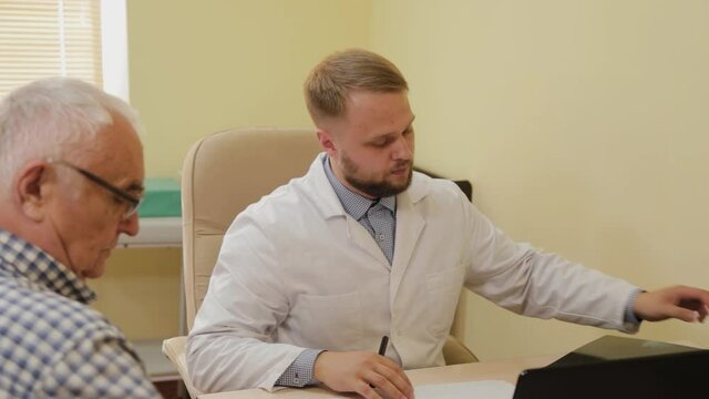 Male neurologist looking at an x-ray picture with an elderly patient.