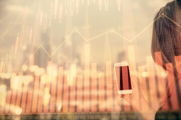 Double exposure of forex chart sketch hologram and woman holding and using a mobile device. Stock market concept.