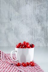 Cornel berries in a cup with picnic cloth side view on grey and white background
