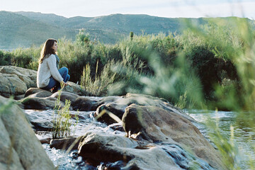 Woman sitting quietly on some rocks in a river at sunrise