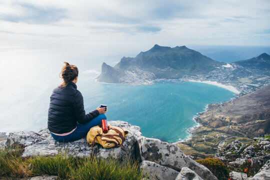 Hiker on a mountain summit enjoying the view and drinking coffee from a thermos flask
