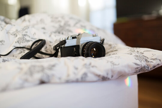 Vintage analogical camera on flowered duvet in bright bedroom with rainbows