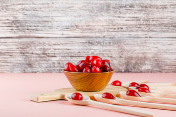 Cornel berries in spoons and bowl with cutting board side view on pink and wooden background