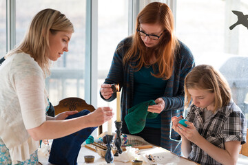 Young girl painting colorful Easter egg designs with older gener