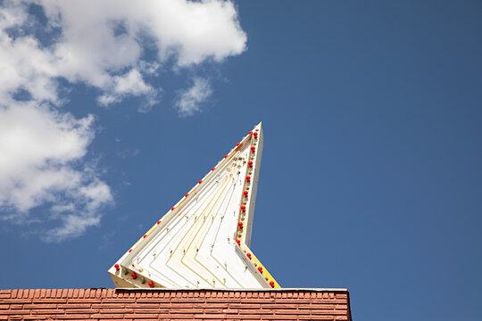 A neon arrow sign sitting on top of a building with blue sky