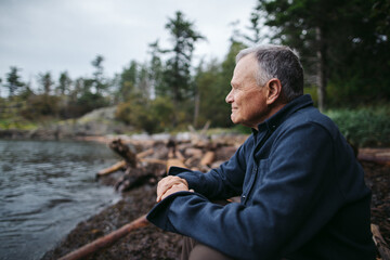 Mature man sitting on beach log alone.