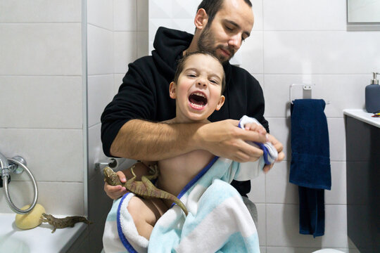 Baby boy screaming while his father tries to dry him with a towel