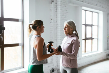 Young trainer giving dumbbells to mature woman