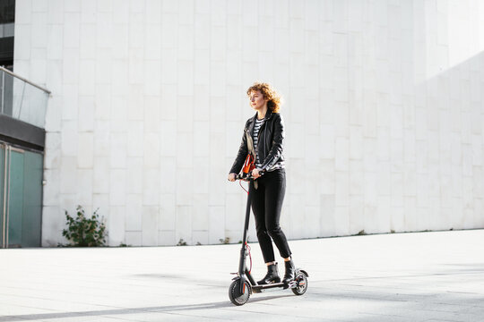Stylish woman riding electric scooter in modern city