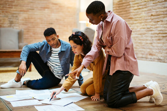 Group of young business people sitting on floor and discussing documents