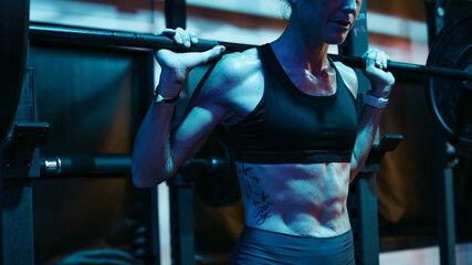 Sweaty athlete woman training hard in dark, moody gym.