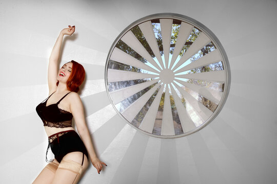 Woman dancing by a wall and a circular window wearing lingerie closing her eyes. 