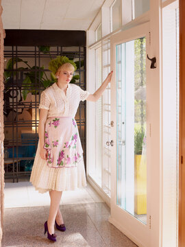 Vintage Woman standing in hallway by the front door looking at the ground in a mid century house. Dallas, TX