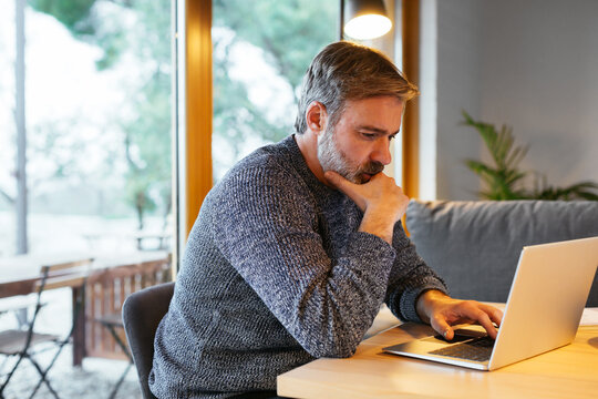 Focused adult man using laptop at home office.
