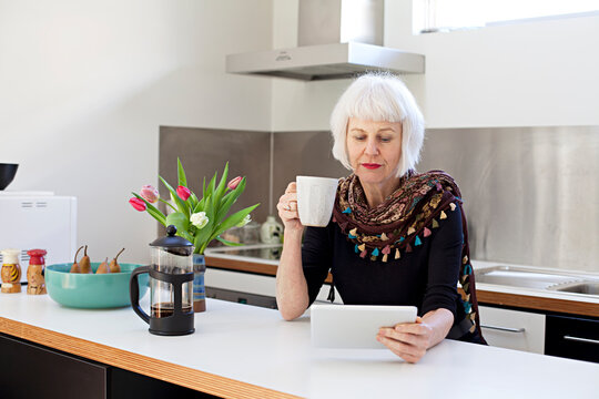 Senior woman in kitchen with coffee using touchpad