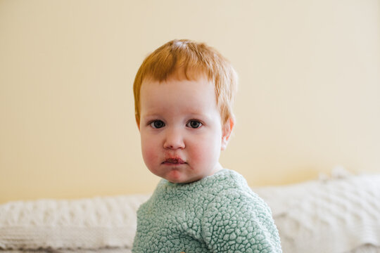 Serious and thoughtful toddler baby with red hair at home,