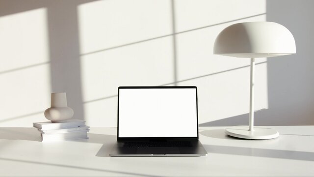 A photo of a black laptop on a white desk with a lamp and books
