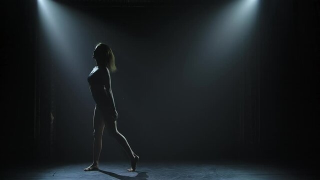 Woman dancing modern dance at smoky stage with spotlights. Vogue or contemporary dance. Young dancer performing on dark stage.