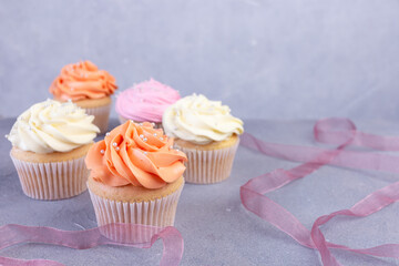 Cupcakes with pink, orange, white cream decorated with ribbon. Selective focus. Birthday celebration concept.