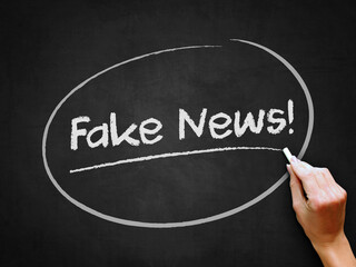 A hand writing 'Fake News!' on chalkboard for untrue or hoax news theme.