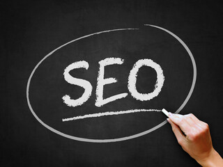A hand writing 'SEO' on chalkboard for internet or online search engine optimization theme.