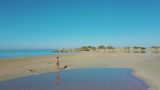 drone aerial view of woman walking in empty elafonissi beach lagoon reflection of blue clear sky