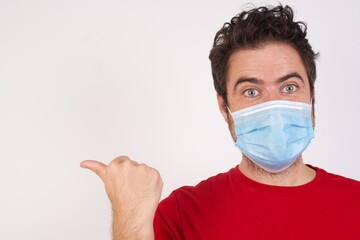 Lovely Young caucasian man with short hair wearing medical mask standing over isolated white background pointing aside with forefinger, showing at copy space having news about bargains
