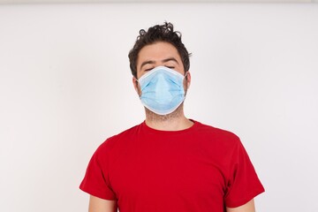 Young caucasian man with short hair wearing medical mask standing over isolated white background looking sleepy and tired, exhausted for fatigue and hangover, lazy eyes in the morning.