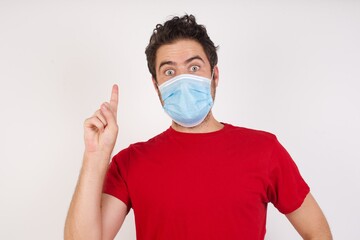 Young caucasian man with short hair wearing medical mask standing over isolated white background holding finger up having idea and posing