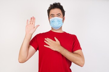 Young caucasian man with short hair wearing medical mask standing over isolated white background Swearing with hand on chest and open palm, making a loyalty promise oath
