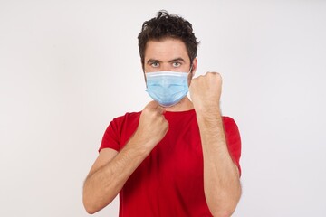 Young caucasian man with short hair wearing medical mask standing over isolated white background Ready to fight with fist defense gesture, angry and upset face, afraid of problem.