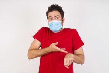 Young caucasian man with short hair wearing medical mask standing over isolated white background In hurry pointing to watch time, impatience, upset and angry for deadline delay.