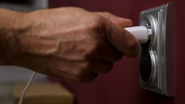 Charging Mobile Phone Battery. Hand plug into electricity socket a power adapter cord usb device mobile phone cell charge