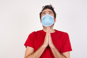 Young caucasian man with short hair wearing medical mask standing over isolated white background begging and praying with hands together with hope expression on face very emotional and worried. Asking