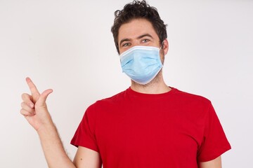 Young caucasian man with short hair wearing medical mask standing over isolated white background pointing up with fingers number eight in Chinese sign language BÄ.