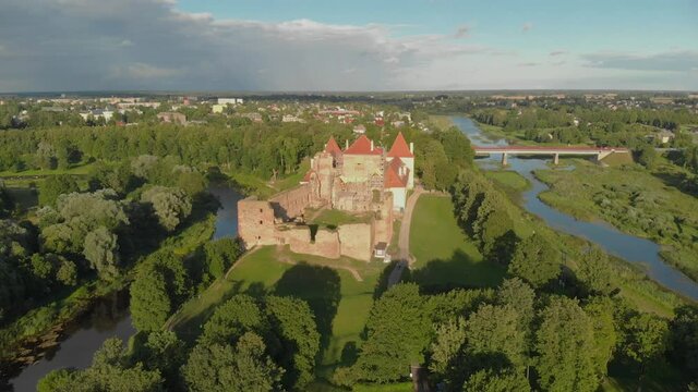 Aerial flying away from Bauska castle in Latvia at golden hour, showing a tourist attraction