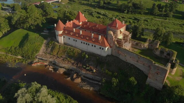 Drone panorama of Bauska castle in Latvia, with scaffolding and ruins next to the restored castle