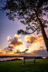 Fototapeta premium Beautiful Sunrise and clouds city view over the river from hill top with a bench and tree 