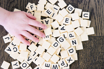 Game tiles with letters dumped onto a table and child's hand reaching for pieces; mixed tiles with the alphabet spilled onto the floor