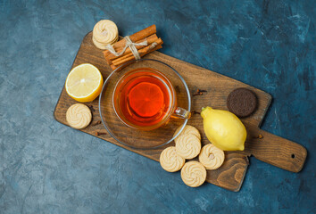 Biscuits with spices, tea, lemon top view on dark blue and cutting board background