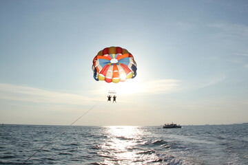 Fototapeta na wymiar A young man and a girl are flying on a double parachute behind a boat over the sea.