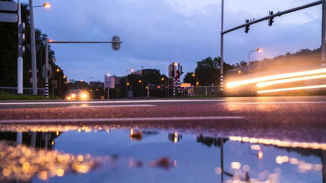 Timelapse of cars stopping at a traffic light and pulling up. It's dusk, headlights are on. The sky is cloudy.