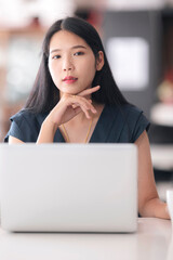 Portrait of young beautiful asian businesswoman smiling and looking at camera while sitting in modern office. Vertical view.