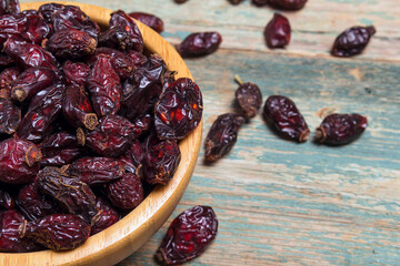 Dried rose hips in a wooden bowl close-up on an old wooden table.