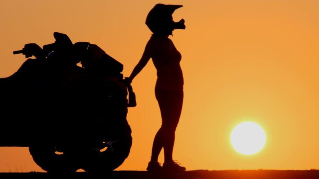 Silhouette of man in helmet sits on quad bike on background of sun during sunset. Woman travels on ATV.