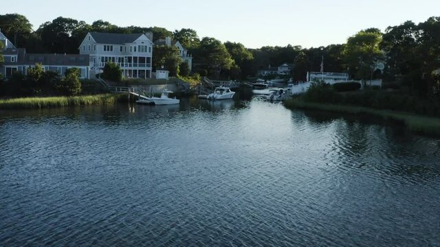 upwards pan on the lake revealing a quaint and beautiful private marina in Cape Cod with boats, houses, and a unique sun flare