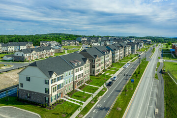 Fototapeta na wymiar Aerial view of a new neighborhood street lined with modern townhouses with colorful facade in the East Coast United States dreamy cloudy blue sky