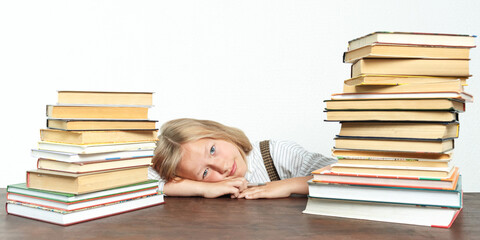 Portrait of a teenage girl lying tired at the table among the books.